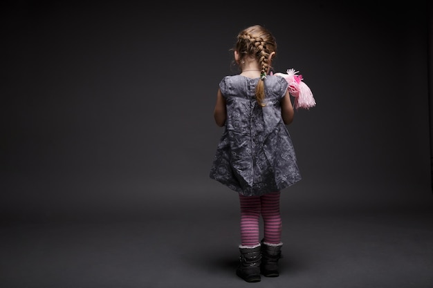 Image arrière d'une petite fille avec un tout-petit poupée offensé par quelqu'un de mauvaise humeur sur fond gris foncé