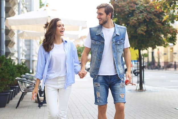 Image d'un beau couple heureux en vêtements d'été souriant et se tenant la main en marchant dans la rue de la ville.