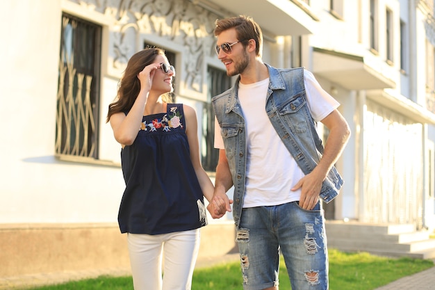 Image d'un beau couple heureux en vêtements d'été souriant et se tenant la main en marchant dans la rue de la ville.