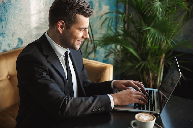 Image d'un beau jeune homme d'affaires heureux assis dans un café à l'aide d'un ordinateur portable.