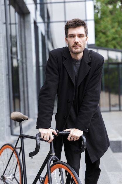 Image de beau jeune homme d'affaires marchant à l'extérieur avec vélo.