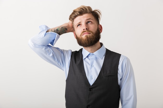 Image d'un beau jeune homme barbu pensant debout isolé sur un mur blanc.