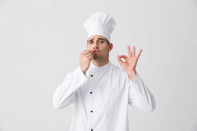 Image de beau jeune homme chef à l'intérieur isolé sur fond de mur blanc.