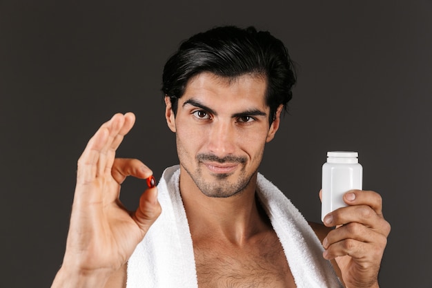 Photo image d'un beau jeune homme isolé avec une serviette tenant des vitamines de pilules.