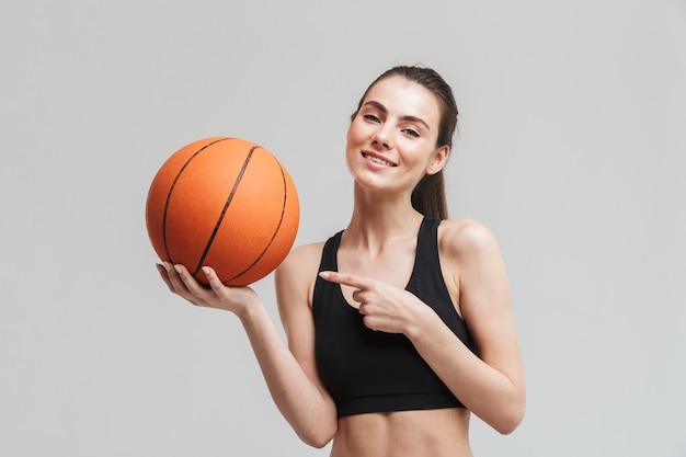 Image d'un beau jeune joueur de basket-ball femme fitness sport posant avec basket-ball isolé sur mur gris.