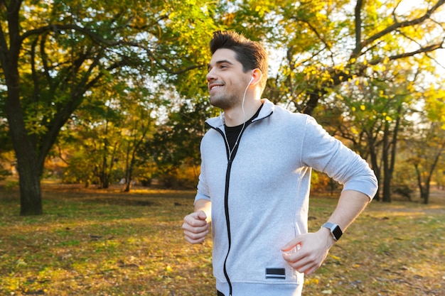 Image d'un beau jeune sportif à l'extérieur dans le parc à l'écoute de la musique avec des écouteurs en cours d'exécution.