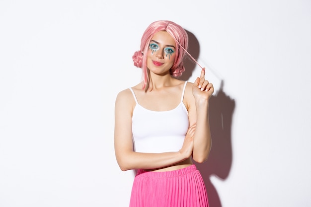 Image d'un beau modèle féminin en tenue d'halloween, portant une perruque rose et des vêtements colorés, souriant à la caméra, debout sur fond blanc.