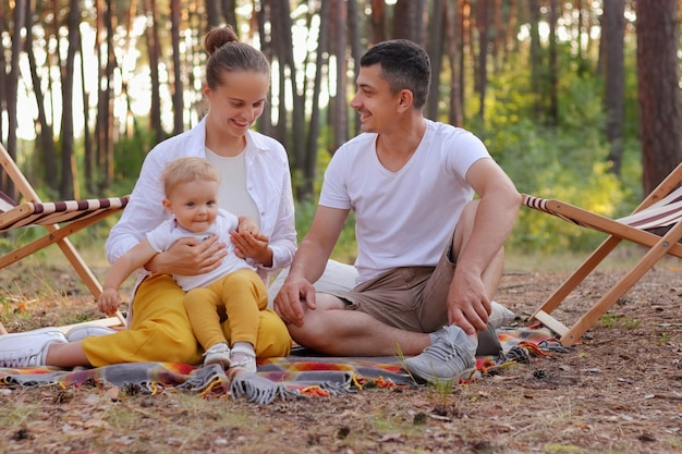 Image d'un beau parent heureux assis dans la forêt avec son tout-petit bébé et s'amusant ensemble en exprimant des émotions positives et du bonheur