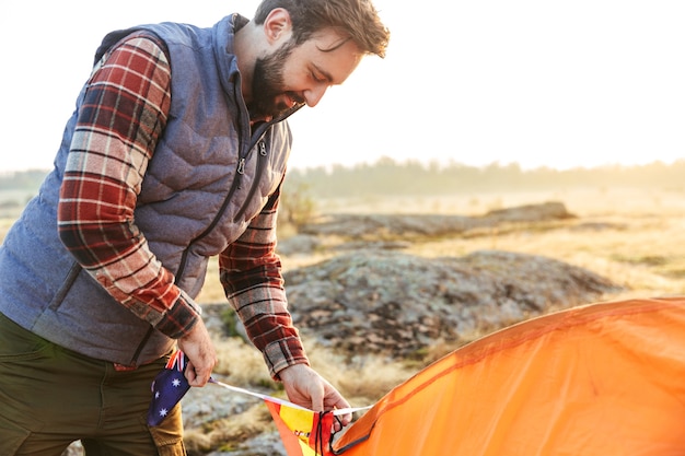 Image d'un bel homme barbu à l'extérieur avec une tente dans un camping de vacances alternatif gratuit.