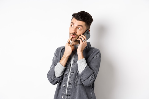 Image d'un bel homme pensif, parler au téléphone et penser, faire un choix tout en faisant l'ordre à emporter, debout sur un fond blanc.