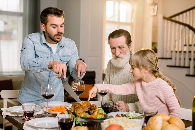 Image de bel homme père montrant comment couper la dinde rôtie à sa petite fille mignonne