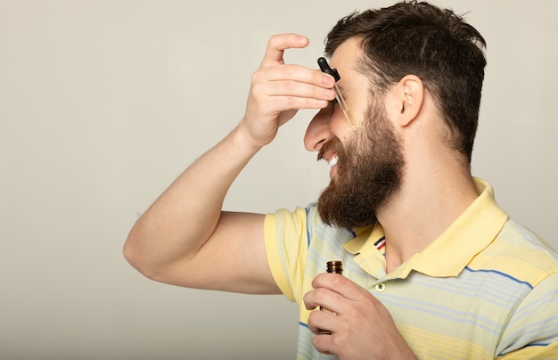 Image d'un bel homme avec pipette avec de l'huile à barbe