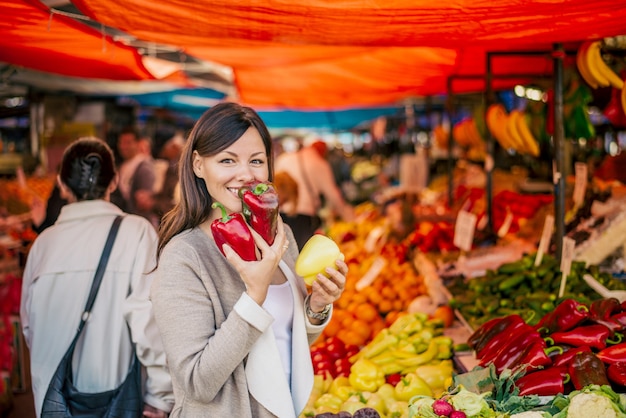 Image d&#39;une belle femme achetant du paprika. Profitant de l&#39;odeur fraîche des légumes.