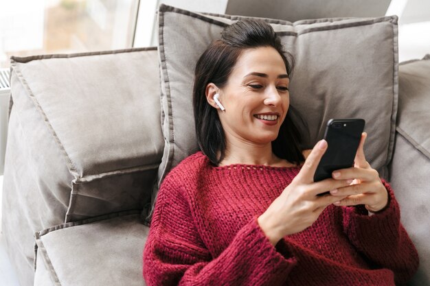 Image d'une belle femme à l'intérieur à la maison sur un canapé à l'aide d'un téléphone mobile.