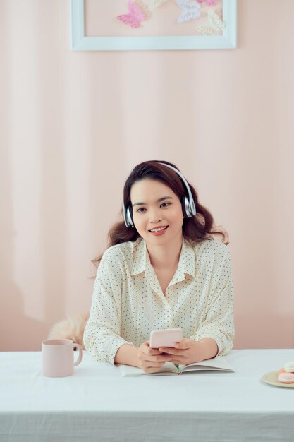 Image d'une belle femme sérieuse utilisant un casque sans fil et un téléphone portable assis à table