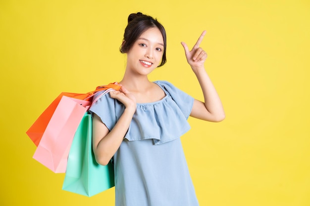 Image d'une belle fille asiatique dans une robe tenant un sac à provisions dans sa main posant sur le fond