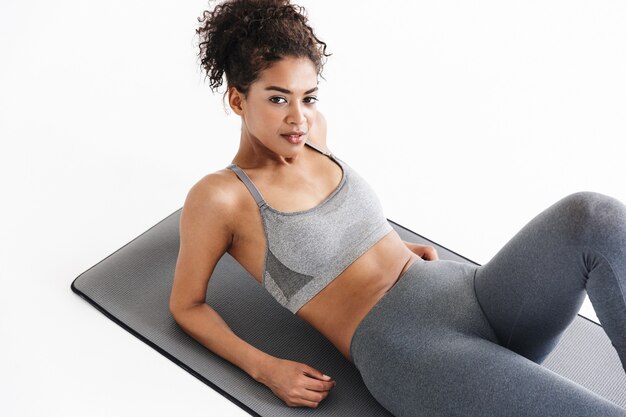 Image d'une belle jeune femme africaine de remise en forme sportive plus forte et étonnante faire des exercices isolés sur un mur blanc.