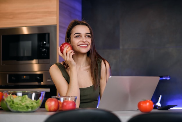 Image d'une belle jeune femme avec apple assis à l'intérieur à l'aide d'un ordinateur portable.