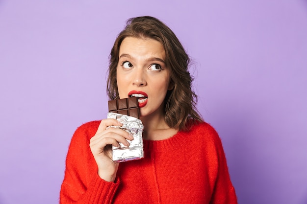 Image d'une belle jeune femme confuse posant isolé sur mur de mur violet tenant du chocolat.