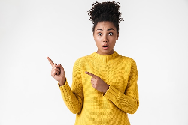 Image d'une belle jeune femme émotionnelle choquée posant sur un mur blanc pointant.