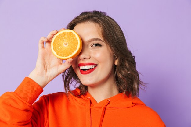 Image d'une belle jeune femme excitée posant isolé sur mur de mur violet tenant des yeux d'agrumes orange couvrant.