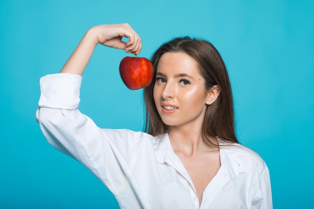 Image d'une belle jeune femme joyeuse à pleines dents posant isolée sur fond bleu tenant une pomme