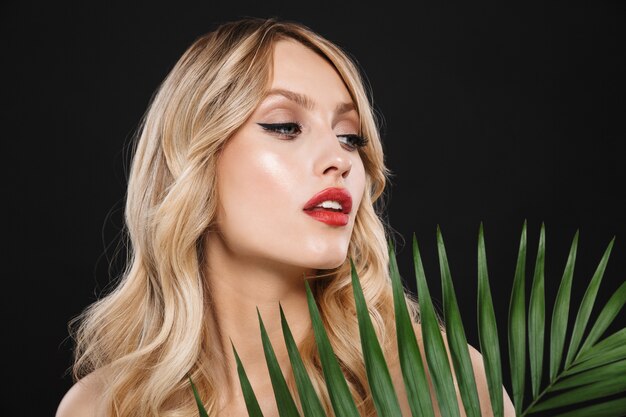 Image de belle jeune femme avec des lèvres rouges maquillage lumineux posant isolé avec fleur verte feuille.