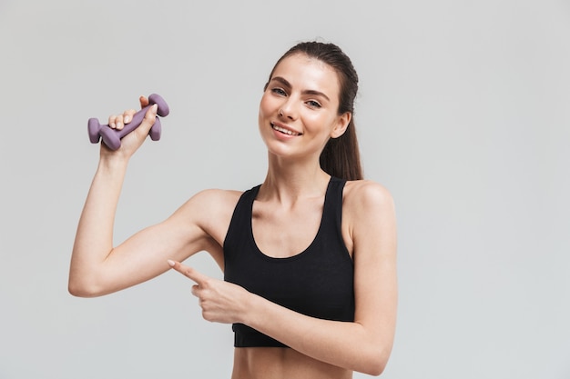 Image d'une belle jeune femme de remise en forme sportive faire des exercices avec des haltères isolés sur un mur gris.