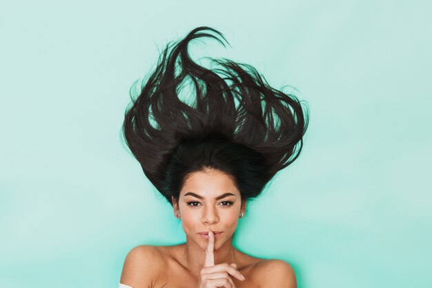 Image de la belle jeune femme se trouve isolé sur la lumière bleue montrant le geste de silence. Concept de cheveux sains.