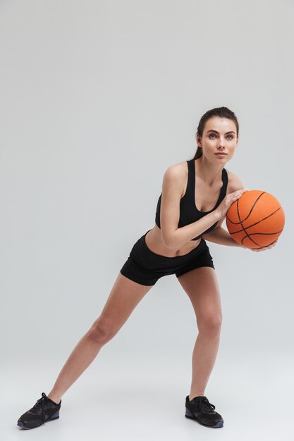 Image d'une belle jeune femme sportive fitness joueur faire des exercices jouer au basket-ball isolé sur mur gris.