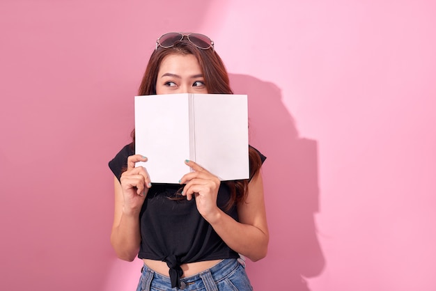 Image de la belle jeune jolie femme posant isolée sur mur rose tenant un livre de lecture.