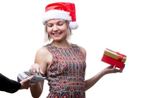 Image d'une blonde heureuse à lunettes et bonnet de noel avec cadeau et main de l'homme avec terminal pour carte bancaire