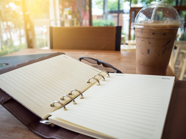 Image de cahier ouvert avec du café glacé et des verres sur une table en bois.