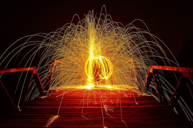 Image d'un cercle entrelacé de lumière jaune et d'étincelles autour d'une personne la nuit sur un pont