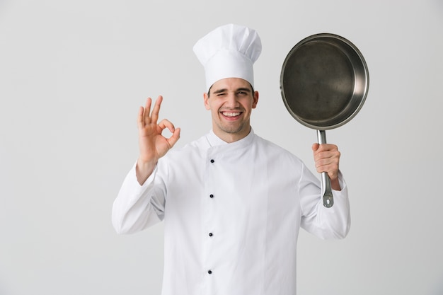 Image de chef jeune homme émotionnel excité à l'intérieur isolé sur fond de mur blanc tenant une poêle à frire.