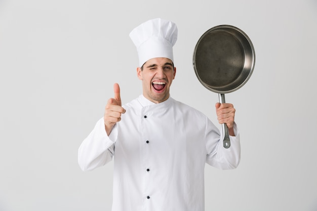 Image de chef jeune homme émotionnel excité à l'intérieur isolé sur fond de mur blanc tenant une poêle à frire.