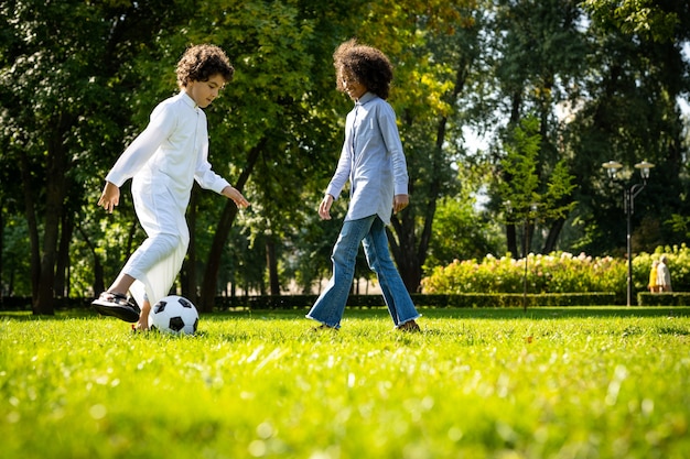Image cinématographique d'une famille des émirats passant du temps au parc. Frère et soeur jouant au football dans l'herbe