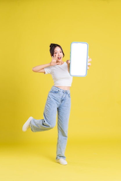 Image complète du corps d'une jeune fille asiatique tenant un téléphone avec un visage joyeux sur fond jaune