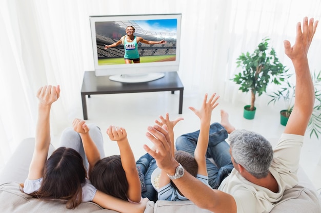 Image composée de famille soulevant leurs bras devant la télévision