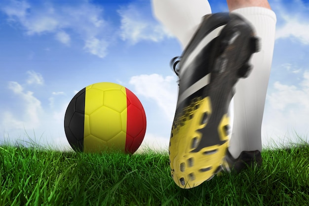 Image composite de la chaussure de football kicking belgique ball contre champ d'herbe sous le ciel bleu