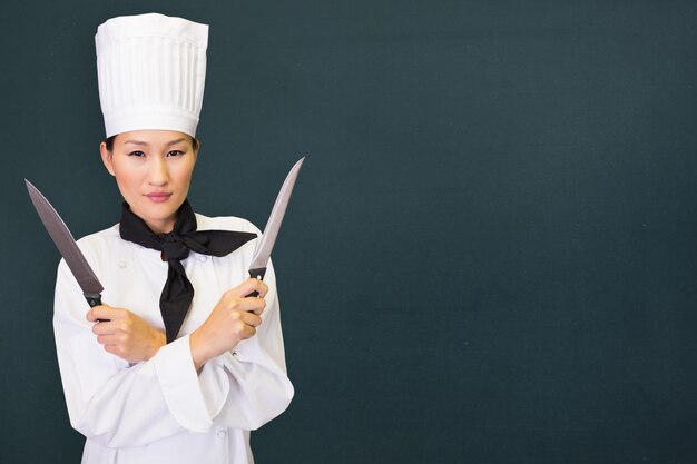 Image composite d'une femme cuisinière confiante tenant des couteaux dans la cuisine