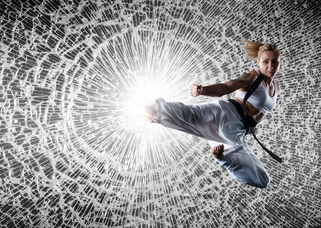 Photo image composite de fille de karaté portant des vêtements de sport blancs et ceinture noire, brisant le verre en saut