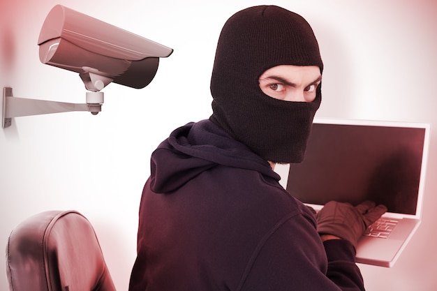 Image composite de hacker assis et pirater un ordinateur portable