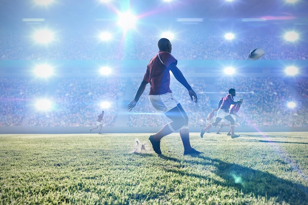 Image composite d'un joueur de rugby donnant un coup de pied dans le ballon à ses coéquipiers sur le terrain