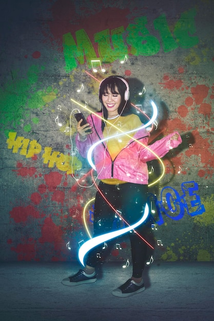 Image composite numérique d'une femme souriante écoutant de la musique sur son téléphone portable contre le mur