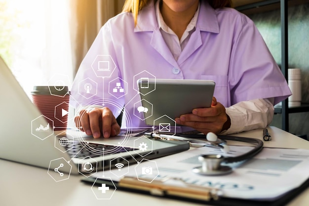 Image composite numérique d'une médecin utilisant un ordinateur portable et une tablette numérique avec divers signes en premier plan