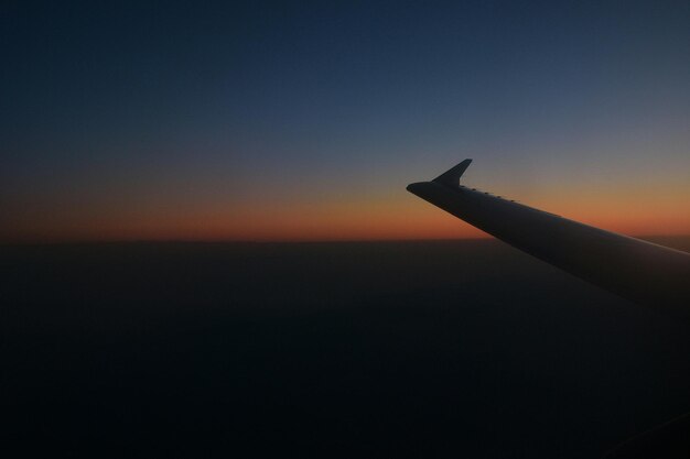 Image coupée d'une aile d'avion volant contre le ciel au coucher du soleil