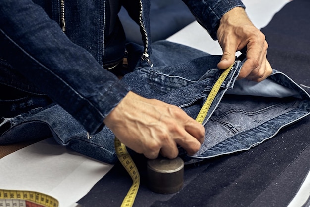 l'image coupée du tailleur fait des mesures de jeans avec un mètre dans un atelier de couture.