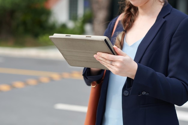 Image coupée d'une femme d'affaires debout à l'extérieur et lisant un rapport sur une tablette