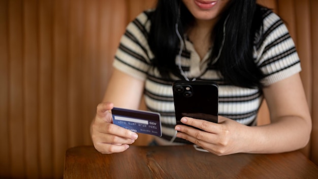 Une image coupée d'une femme asiatique tenant un smartphone et une carte de crédit à une table dans un café